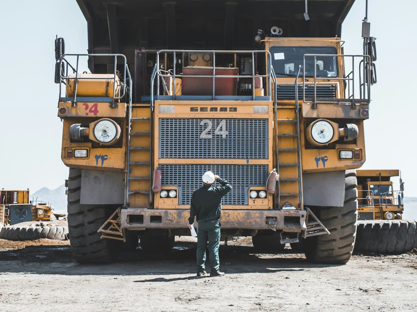 Mine worker in a white hard hat standing in front of a large yellow haul truck