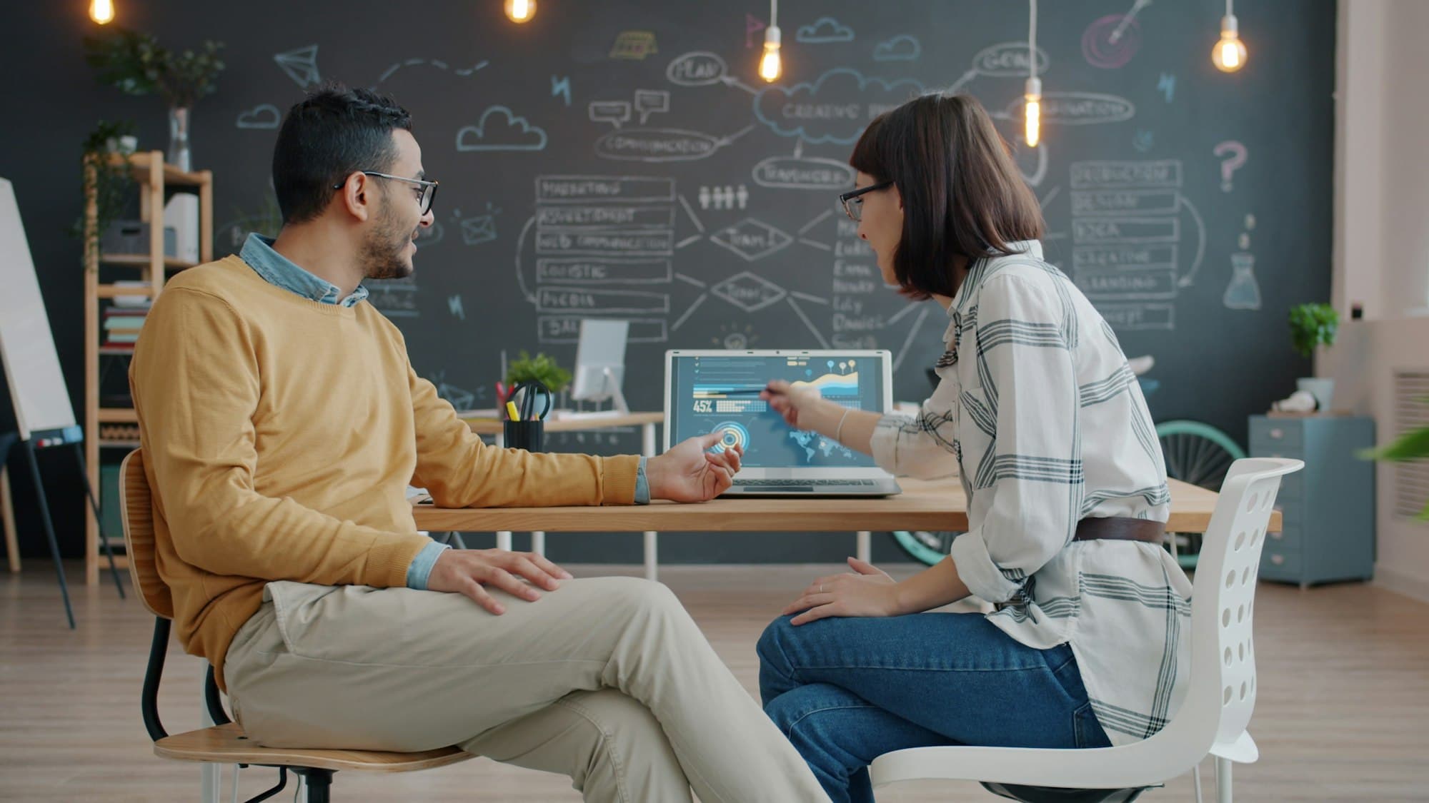 Two colleagues discussing work together at a desk with a laptop