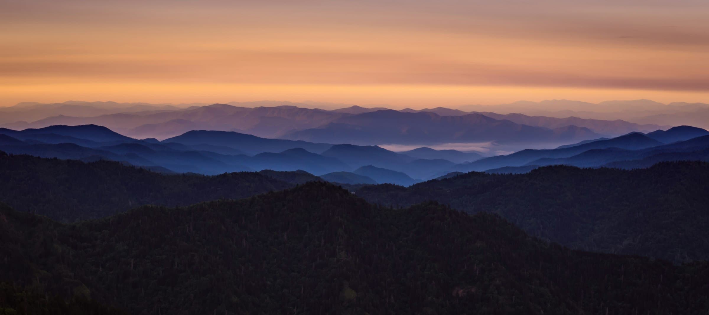 Layered mountain ridges at dusk under a glowing sky